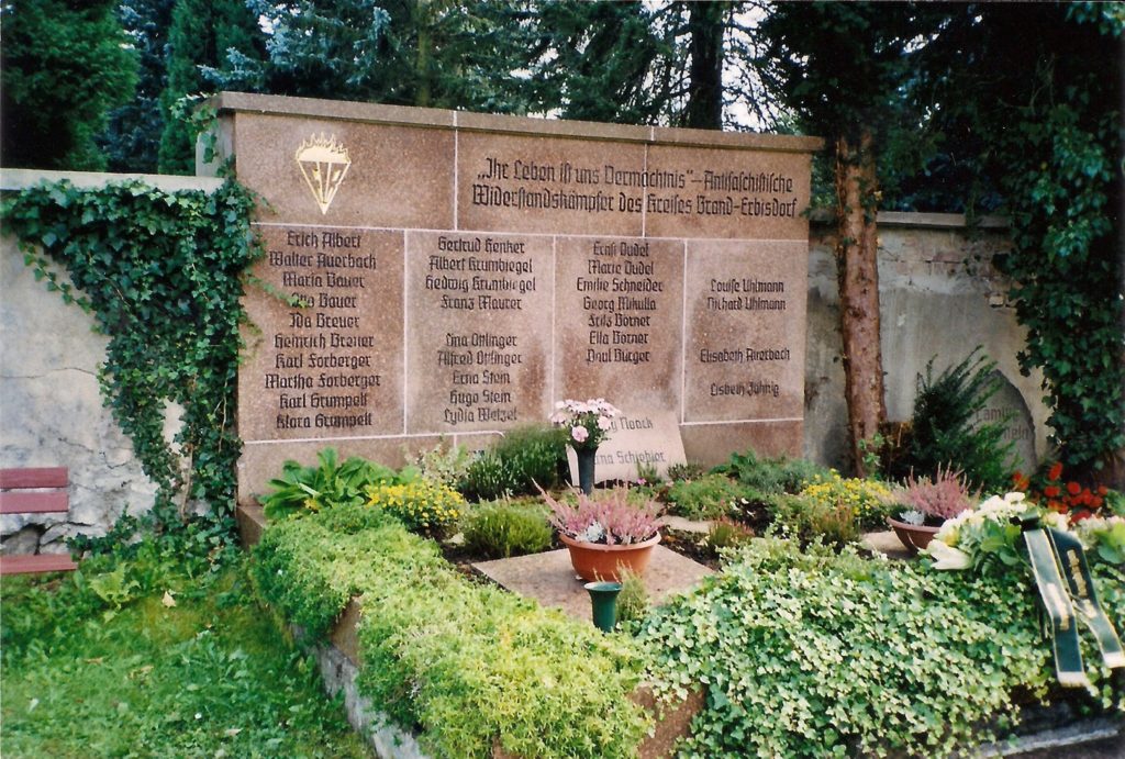 Gedenkstein mit namen der Opfer des Faschismus mit Pflanzen und Blumen im Vordergrund